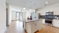 This single-floor residence features a contemporary open-concept layout with clean lines and a bright, neutral palette throughout. The kitchen serves as a central highlight, showcasing white shaker-style cabinetry, quartz-toned countertops, a bold blue-gray subway tile backsplash, and a full suite of stainless steel appliances including a range, over-the-range microwave, and refrigerator. A generously sized center island with pendant lighting overhead provides additional prep and seating space, flowing seamlessly into the adjacent living area. The living space is finished with light hardwood-style flooring, a ceiling fan, and a glass-panel door that invites natural light and outdoor views.

The bedrooms are carpeted for comfort, each equipped with a ceiling fan and windows offering neighborhood views. Two bathrooms serve the unit: a primary bath featuring an extended vanity with dual sinks, gray countertops, white cabinetry, and a glass-enclosed shower, and a secondary bath with a white subway tile walk-in shower, single vanity, and wood-look flooring. The overall design is cohesive and modern, with consistent finishes and a bright, airy ambiance throughout.