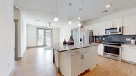 This single-floor residence features a contemporary open-concept layout with clean lines and a bright, neutral palette throughout. The kitchen serves as a central highlight, showcasing white shaker-style cabinetry, quartz-toned countertops, a bold blue-gray subway tile backsplash, and a full suite of stainless steel appliances including a range, over-the-range microwave, and refrigerator. A generously sized center island with pendant lighting overhead provides additional prep and seating space, flowing seamlessly into the adjacent living area. The living space is finished with light hardwood-style flooring, a ceiling fan, and a glass-panel door that invites natural light and outdoor views.

The bedrooms are carpeted for comfort, each equipped with a ceiling fan and windows offering neighborhood views. Two bathrooms serve the unit: a primary bath featuring an extended vanity with dual sinks, gray countertops, white cabinetry, and a glass-enclosed shower, and a secondary bath with a white subway tile walk-in shower, single vanity, and wood-look flooring. The overall design is cohesive and modern, with consistent finishes and a bright, airy ambiance throughout.