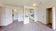 This single-floor unit offers a practical and well-organized layout across several rooms. The living area is carpeted and open, connecting directly to the kitchen via a half-wall peninsula that provides a pass-through counter with a sink. The kitchen is equipped with white appliances, including a refrigerator, microwave, and electric range, alongside cabinetry with wood-toned accents and tile flooring. A sliding glass door fitted with vertical blinds in the living area allows natural light to enter and provides outdoor access. The bedrooms are carpeted and feature neutral walls, each with windows fitted with blinds that allow natural light while maintaining privacy. The unit includes two bathrooms: one features a standalone walk-in shower with a frosted glass door and chrome frame, accompanied by a vanity and toilet; the second bathroom offers a full shower-tub combo with a curtain rod, vanity with mirror, and toilet. Throughout the unit, the color palette remains consistent with soft beige and white tones, contributing to a clean, understated aesthetic. The single-floor design ensures ease of navigation throughout the space.