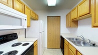 Located at 4111 Wincove Dr in Groveport, Ohio, this single-floor residence offers a practical and well-organized layout designed for comfortable everyday living. The kitchen is a standout feature, designed in a classic galley configuration that maximizes efficiency and storage. Warm honey-toned oak cabinetry lines both walls, providing generous storage space for pantry items and cookware. The kitchen is equipped with a full suite of white appliances, including an electric coil range with oven, a built-in microwave, a full-size refrigerator, and a dishwasher. A double-basin stainless steel sink sits beneath upper cabinets on one side, while light-toned countertops run the length of both walls. The flooring features neutral vinyl tile that is easy to maintain. A flush-mounted overhead light fixture provides consistent illumination throughout the kitchen. A wood-paneled bi-fold closet door at the end of the kitchen corridor offers additional storage or pantry access. The overall aesthetic is clean, neutral, and functional, making it a practical space suited for a variety of residents.