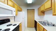 Located at 4111 Wincove Dr in Groveport, Ohio, this single-floor residence offers a practical and well-organized layout designed for comfortable everyday living. The kitchen is a standout feature, designed in a classic galley configuration that maximizes efficiency and storage. Warm honey-toned oak cabinetry lines both walls, providing generous storage space for pantry items and cookware. The kitchen is equipped with a full suite of white appliances, including an electric coil range with oven, a built-in microwave, a full-size refrigerator, and a dishwasher. A double-basin stainless steel sink sits beneath upper cabinets on one side, while light-toned countertops run the length of both walls. The flooring features neutral vinyl tile that is easy to maintain. A flush-mounted overhead light fixture provides consistent illumination throughout the kitchen. A wood-paneled bi-fold closet door at the end of the kitchen corridor offers additional storage or pantry access. The overall aesthetic is clean, neutral, and functional, making it a practical space suited for a variety of residents.
