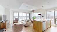 Located at 1240-1250 Cummings Ave in Ottawa, this well-appointed 2-bedroom, 1-bathroom unit offers a thoughtfully designed open-concept layout with modern finishes throughout. The combined kitchen and living area serves as the heart of the home, bathed in abundant natural light from expansive floor-to-ceiling windows that frame sweeping city views. The kitchen features a clean, contemporary aesthetic with two-tone cabinetry — white upper cabinets paired with warm wood lower cabinets — stainless steel appliances, a white quartz countertop, and a functional island with an integrated sink. The living area is bright and airy, with light hardwood flooring that carries through the entire unit. The primary bedroom benefits from a large window overlooking the city skyline, while the second bedroom offers a sliding door closet and a calm, minimalist atmosphere. The bathroom is finished with elegant marble-look tile flooring, a glass-enclosed shower, and a stacked in-unit washer and dryer for added convenience. A clean, light-filled hallway with recessed lighting and a sleek sliding door connects the spaces seamlessly, completing this modern and functional urban residence.