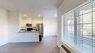 This single-floor unit offers a clean, functional layout with a modern aesthetic throughout. The open-concept kitchen flows naturally into the living area, creating a cohesive and practical living space. The kitchen is well-appointed with white shaker-style cabinetry, dark countertops, and a full suite of stainless steel appliances, including a refrigerator, stove, and built-in microwave. Wood-style flooring extends throughout the main living and kitchen areas, lending a warm, contemporary feel.

The living area is generously sized and benefits from natural light provided by large windows fitted with horizontal blinds, offering outdoor views of surrounding greenery. A wall-mounted HVAC unit provides climate control. A dedicated laundry area with a stacked washer and dryer is conveniently tucked within the unit.

The bedroom features soft carpeting, a sliding-door closet offering ample storage, and its own window for natural light. The bathroom is finished with tile flooring, a full soaking tub with shower, a white vanity with dark countertop, and a wall-mounted mirror. Throughout, the neutral color palette and clean finishes contribute to a bright, move-in-ready atmosphere.