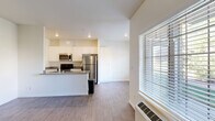 This single-floor unit offers a clean, functional layout with a modern aesthetic throughout. The open-concept kitchen flows naturally into the living area, creating a cohesive and practical living space. The kitchen is well-appointed with white shaker-style cabinetry, dark countertops, and a full suite of stainless steel appliances, including a refrigerator, stove, and built-in microwave. Wood-style flooring extends throughout the main living and kitchen areas, lending a warm, contemporary feel.

The living area is generously sized and benefits from natural light provided by large windows fitted with horizontal blinds, offering outdoor views of surrounding greenery. A wall-mounted HVAC unit provides climate control. A dedicated laundry area with a stacked washer and dryer is conveniently tucked within the unit.

The bedroom features soft carpeting, a sliding-door closet offering ample storage, and its own window for natural light. The bathroom is finished with tile flooring, a full soaking tub with shower, a white vanity with dark countertop, and a wall-mounted mirror. Throughout, the neutral color palette and clean finishes contribute to a bright, move-in-ready atmosphere.