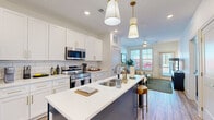 This thoughtfully designed 1-bedroom, 1-bathroom residence offers a seamless open-concept layout that integrates the kitchen and living area into a cohesive, functional living space. The kitchen is a standout feature, showcasing crisp white shaker cabinetry with gold hardware, a white subway tile backsplash, quartz countertops, and a full suite of stainless steel appliances including a French door refrigerator, microwave, and range. A contrasting navy kitchen island with seating provides an ideal spot for casual dining, while stylish pendant lighting adds a modern touch overhead. The living area is bright and welcoming, benefiting from large windows and a glass door that invite ample natural light and provide outdoor views. A ceiling fan enhances comfort throughout. The bedroom is a calm retreat, carpeted for warmth and comfort, featuring multiple windows on two walls that flood the room with natural light. A dedicated walk-in closet offers extensive wire shelving and hanging space for organized storage. The bathroom is clean and modern, with white cabinetry accented by gold hardware, wood-look flooring, and a tub-shower combination. Wood-look flooring flows throughout the main living areas, tying the space together with a warm, contemporary aesthetic.