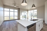 Located on Forevergreen Road in Tiffin, Iowa, this well-designed 2-bedroom, 2-bathroom residence offers a clean, contemporary aesthetic across a single floor. Light hardwood flooring flows seamlessly throughout, complementing the neutral warm and cool tones found in every room.

The heart of the home is a fully integrated open-concept kitchen, dining, and living area. The kitchen features white shaker cabinetry, quartz countertops, stainless steel appliances, and a large center island with a built-in sink — all illuminated by stylish pendant lighting and elevated ceilings that enhance the sense of openness.

The living area is a standout, boasting floor-to-ceiling windows on multiple walls and a sliding glass door that opens to a private balcony, flooding the space with natural light and offering expansive views of the surrounding Iowa landscape.

The spacious primary bedroom includes a generous closet and an en suite bathroom with white cabinetry, quartz countertops, a tall linen tower, and dual mirrors. The second bedroom features large windows with open views and a double-door closet. A second full bathroom with a tub/shower combo and quartz vanity serves the remaining rooms. Additional features include a dedicated laundry area, utility room, and ample closet storage throughout.