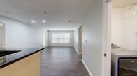 This 1,660 square foot single-story residence at 7205 Inwood Dr in Woburn, MA offers 2 bedrooms and 2 bathrooms across a well-designed, functional floor plan. Throughout the home, consistent wood-style laminate flooring and neutral gray walls create a clean, cohesive aesthetic. The spacious living room features large windows with horizontal blinds that allow ample natural light, along with a sliding door providing outdoor access. The adjacent kitchen-living area is equipped with cream cabinetry, dark granite countertops, a tile backsplash, stainless steel appliances including a gas range, microwave, and refrigerator, and recessed lighting. The primary bedroom measures 180 square feet and includes a ceiling fan and a sizable window. The second bedroom also features multiple windows, ensuring bright, airy conditions. Both bathrooms are finished with white vanities, large mirrors, and vanity lighting; one includes a tub/shower combination with tiled surround. A dedicated laundry room houses side-by-side washer and dryer units alongside built-in wire shelving for additional storage. A connecting hallway ties all rooms together efficiently, completing this practical and modern single-level home.