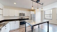 Located in the heart of downtown Detroit on Griswold Street, this one-bedroom, one-bathroom residence offers a well-designed layout with a cohesive blend of modern finishes and urban character. Herringbone-patterned hardwood flooring runs throughout the entire unit, adding a refined, eye-catching detail that ties each room together.

The open living area is bathed in natural light through large, black-framed windows that frame sweeping views of Detroit's iconic downtown skyline. The airy, neutral-toned walls complement the warm flooring and create a bright, welcoming ambiance throughout the space.

The kitchen is a standout feature, showcasing crisp white cabinetry, dark granite countertops, and a full suite of stainless steel appliances including a refrigerator, range, and microwave. A substantial stainless steel kitchen island on casters serves as both a functional prep surface and a striking industrial centerpiece, while Edison-bulb pendant lights overhead add a warm, modern-industrial touch. Open metal shelving provides additional storage and display space.

The bedroom is a comfortable and well-proportioned retreat, with a large window offering city views and generous wall space. The bathroom features a glass-enclosed tiled shower and built-in shelving for added storage convenience. This residence delivers a polished urban living experience in one of Detroit's most vibrant downtown locations.