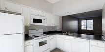 Located at 8181 Herald Cove in Blacklick, Ohio, this two-story home offers a practical and well-organized layout spread across two levels. The kitchen is a standout feature, showcasing crisp white cabinetry that extends toward the ceiling, providing generous storage throughout. Dark countertops create a clean contrast against the white cabinets and appliances, which include a coil-top electric range, over-the-range microwave, refrigerator, and a double-basin sink positioned beneath a window that allows natural light to filter in. The elevated ceiling height in the kitchen adds a sense of openness and airiness to the space. Neutral gray and dark accent walls contribute to a modern, understated aesthetic throughout. The two-story design of the home offers functional separation between living and sleeping areas, providing versatility for a variety of living arrangements. The overall design palette — featuring neutral tones, clean lines, and practical finishes — creates a cohesive and move-in-ready environment suited for everyday living.