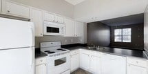 Located at 8181 Herald Cove in Blacklick, Ohio, this two-story home offers a practical and well-organized layout spread across two levels. The kitchen is a standout feature, showcasing crisp white cabinetry that extends toward the ceiling, providing generous storage throughout. Dark countertops create a clean contrast against the white cabinets and appliances, which include a coil-top electric range, over-the-range microwave, refrigerator, and a double-basin sink positioned beneath a window that allows natural light to filter in. The elevated ceiling height in the kitchen adds a sense of openness and airiness to the space. Neutral gray and dark accent walls contribute to a modern, understated aesthetic throughout. The two-story design of the home offers functional separation between living and sleeping areas, providing versatility for a variety of living arrangements. The overall design palette — featuring neutral tones, clean lines, and practical finishes — creates a cohesive and move-in-ready environment suited for everyday living.