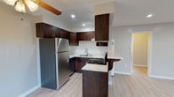 This single-floor residence offers a thoughtfully designed layout that balances functional living spaces with modern finishes. The kitchen serves as a central highlight, showcasing rich dark-espresso shaker cabinets that extend to the ceiling, light stone-look countertops, a stainless steel refrigerator, a gas range with a ventilation hood, and a double-basin sink. A peninsula with a curved countertop overhang provides additional workspace and casual seating, seamlessly connecting the kitchen to the open living and dining areas.

The living area is generously proportioned, featuring large windows dressed with white horizontal blinds that invite abundant natural light. Light wood-style flooring runs consistently throughout the space, lending a clean, cohesive aesthetic. Ceiling fans are present in multiple rooms, contributing both comfort and visual continuity.

The bedrooms are well-sized, each equipped with wall-unit HVAC systems and windows offering outdoor views. One bedroom features a walk-in closet, adding practical storage. The bathroom is clean and functional, offering a full tub-shower combination with a curved rod, white tile surround, a small window for ventilation, and light countertops complementing the dark vanity cabinetry. Overall, the space presents a fresh, move-in-ready atmosphere with consistent modern touches throughout.