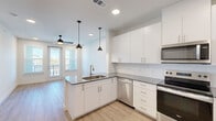 Located at 4600 East McKinney Street in Denton, TX, this 2-bedroom, 1-bathroom residence offers a thoughtfully designed single-floor layout with contemporary finishes throughout. The open-concept kitchen is a standout feature, showcasing crisp white shaker cabinetry, granite countertops, a peninsula with an undermount sink, stylish pendant lighting, and a full suite of stainless steel appliances including a refrigerator, range, microwave, and dishwasher. Light wood-look flooring runs through the main living areas, adding warmth and continuity to the space. The living area is bright and airy, featuring recessed lighting, a ceiling fan, and direct access to a private balcony through a glass-paned door flanked by large windows. Both bedrooms are carpeted and include ceiling fans and ample natural light from double windows. The primary bedroom connects to a well-sized walk-in closet with built-in shelving and hanging rods. The shared bathroom is generously proportioned, offering a granite-topped double vanity with white cabinetry, wood-look flooring, and a full soaking tub with shower. A second closet provides additional storage. The unit's clean, modern aesthetic is consistent throughout, making it a functional and attractive living space.