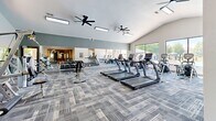 Located at 2426 Thoroughbred Dr in Bowling Green, Kentucky, this fitness center is a comprehensive, single-floor facility divided into two distinct exercise rooms designed to support a wide range of workout routines.

The main exercise area is a generously proportioned space featuring vaulted ceilings, dual ceiling fans, and large floor-to-ceiling windows that flood the room with natural light and offer direct views of the outdoor pool. This room is equipped with a full row of TRUE treadmills, elliptical cross-trainers, a dumbbell rack, and a dedicated TKO functional training rig complete with cable systems, a monkey bar overhead ladder, TRX suspension straps, and a heavy bag. Patterned carpet tiles cover the floor throughout, and wall-length mirrors enhance the sense of space. A hydration station with a water fountain is conveniently accessible nearby.

The second exercise room serves as a dedicated cycling and stretching studio with smooth hardwood-style flooring, recessed lighting, and wall-mounted flat-screen displays for guided workouts. This room also features a medicine ball rack, a stationary bike, and additional windows overlooking the pool area. Together, the two rooms create a cohesive, full-featured fitness environment suited for cardio, strength, functional training, and group cycling activities.