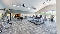 Located at 2426 Thoroughbred Dr in Bowling Green, Kentucky, this fitness center is a comprehensive, single-floor facility divided into two distinct exercise rooms designed to support a wide range of workout routines.

The main exercise area is a generously proportioned space featuring vaulted ceilings, dual ceiling fans, and large floor-to-ceiling windows that flood the room with natural light and offer direct views of the outdoor pool. This room is equipped with a full row of TRUE treadmills, elliptical cross-trainers, a dumbbell rack, and a dedicated TKO functional training rig complete with cable systems, a monkey bar overhead ladder, TRX suspension straps, and a heavy bag. Patterned carpet tiles cover the floor throughout, and wall-length mirrors enhance the sense of space. A hydration station with a water fountain is conveniently accessible nearby.

The second exercise room serves as a dedicated cycling and stretching studio with smooth hardwood-style flooring, recessed lighting, and wall-mounted flat-screen displays for guided workouts. This room also features a medicine ball rack, a stationary bike, and additional windows overlooking the pool area. Together, the two rooms create a cohesive, full-featured fitness environment suited for cardio, strength, functional training, and group cycling activities.