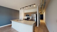 This one-bedroom, one-bathroom unit in Memphis, Tennessee offers a thoughtfully designed open-concept layout that blends modern finishes with industrial-inspired character. Light wood-tone flooring flows throughout the space, complementing the clean white walls and bold dark accent walls that add depth and visual interest to the living areas.

The kitchen is a standout feature, anchored by a large peninsula with a granite countertop and an undermount sink — ideal for meal prep or casual dining. Taupe cabinetry pairs with a full suite of stainless steel appliances, including a refrigerator, range, and built-in microwave. Overhead, an exposed spiral ductwork element and a track lighting system contribute to the space's urban, loft-like aesthetic.

The open living area is bright and airy, benefiting from a row of large windows that invite natural light and offer views of the surrounding neighborhood. The exposed ductwork continues here, reinforcing the industrial design theme.

The bedroom is a quiet, neutral retreat featuring warm wood-tone flooring, crisp white walls, and a ceiling fan with integrated lighting. The layout provides a comfortable and functional private space within the unit.

Throughout, the design strikes a balance between contemporary finishes and industrial character, creating a cohesive and inviting atmosphere.
