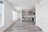This modern single-floor unit offers a clean, contemporary design with consistent wood-style plank flooring running throughout every room, tying the space together with a cohesive, neutral aesthetic. The open-concept layout connects the living area to the kitchen, creating a generous and functional shared space. Large windows line the living area, filling the room with abundant natural light and offering views of the surrounding neighborhood.

The kitchen is well-appointed with sleek, high-gloss cabinetry in a warm taupe finish extending to the ceiling for maximum storage. A full suite of stainless steel appliances includes a refrigerator, electric range, over-the-range microwave, and dishwasher. Light countertops and a clean tile backsplash complete the polished look.

Two bedrooms provide comfortable accommodations, each featuring large windows that frame outdoor views and flood the rooms with natural light. One bedroom includes a ceiling fan and a spacious sliding-door closet. The unit also includes a dedicated entry area with a secure door.

The full bathroom is neatly designed with a shower/tub combination, a wall-mounted vanity with an undermount sink, and warm-toned flooring. A stacked in-unit washer and dryer adds everyday convenience. Throughout, the space maintains a bright, minimalist character well-suited for modern living.