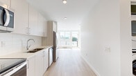 This thoughtfully designed 1-bedroom, 1-bathroom unit offers a clean, modern aesthetic across a single floor. The open-concept layout seamlessly connects the kitchen and living area, creating a bright and airy atmosphere enhanced by light-toned luxury vinyl plank flooring throughout. The kitchen is outfitted with crisp white flat-panel cabinetry, light wood accents, stainless steel appliances including a refrigerator, dishwasher, and microwave, as well as a sleek undermount sink — all contributing to a functional and stylish culinary space. Recessed lighting illuminates the interior, while large windows at the end of the living area flood the space with natural light and frame views of the surrounding treetops and neighbourhood. The generously sized primary bedroom is a standout feature, offering ample space, large windows that invite in natural light, and warm hardwood-style flooring. The full bathroom is finished with warm wood-tone cabinetry, a wide vanity mirror, and a curved shower rod, maintaining the unit's consistent contemporary style. A hallway connects the rooms efficiently, adding to the unit's practical flow. The overall ambiance is fresh, clean, and move-in ready.