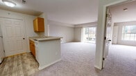The Lancaster in Trenton, Michigan presents a thoughtfully laid-out 2-bedroom, 2-bathroom residence on a single floor. The open-concept living and dining area is bright and welcoming, featuring plush wall-to-wall carpeting, neutral-toned walls, and a large sliding glass door that fills the space with natural light and provides outdoor views. A peninsula-style kitchen overlooks the living area, creating a connected and functional layout. The galley kitchen is equipped with warm oak cabinetry, white appliances including a range, refrigerator, dishwasher, and built-in microwave, along with a double sink and wood-look vinyl flooring. Both bedrooms are comfortably sized, carpeted, and receive natural light through well-positioned windows with outdoor views. One bedroom includes direct access to a closet and an adjoining bathroom. Each of the two full bathrooms features oak vanity cabinetry, a single-basin sink with light countertops, a tub-shower combination with tiled surround, and wood-look flooring. The home's consistent use of neutral tones and natural materials creates a clean, cohesive aesthetic throughout, offering a comfortable and functional living environment in a well-established community.