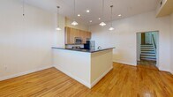 Located at 209 E Main St in the heart of downtown Richmond, Virginia, this single-floor unit offers a well-designed layout with consistent hardwood flooring throughout. The open-concept kitchen is a standout feature, equipped with stainless steel appliances including a refrigerator, microwave, and range, complemented by light wood cabinetry and dark granite countertops. A peninsula with a breakfast bar separates the kitchen from the adjoining living area, while stylish pendant lighting above adds a polished touch. Recessed lighting throughout the main living space enhances the bright, airy atmosphere. The bedrooms are generously proportioned, each featuring warm hardwood floors and ceiling fans for year-round comfort. The full bathroom is finished with tile flooring, a granite-topped vanity, and a tub-shower combination. A dedicated laundry area with a stacked washer and dryer unit adds everyday convenience, situated alongside a closet with wire shelving for ample storage. The unit's neutral color palette and clean architectural lines create a versatile backdrop suitable for a variety of interior styles. Its prime downtown Richmond location places residents within close proximity to local dining, entertainment, and cultural amenities.