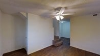 This two-floor residence offers a practical and comfortable layout with a distinct split-level design that adds architectural interest. The main living area features rich, dark hardwood flooring that extends throughout the space, creating a warm and cohesive aesthetic. A ceiling fan with an integrated light fixture is centrally positioned overhead, providing both air circulation and ambient lighting. The textured popcorn ceiling adds a classic touch to the interior.

A set of carpeted stairs serves as the focal transition point between levels, connecting the main living space to an additional area just steps above, which itself leads further into the home's second floor. The neutral white walls throughout provide a clean, versatile backdrop that suits a variety of furnishing styles. The open sightlines between spaces contribute to a sense of flow and connectivity throughout the home.

The layout is designed to separate functional zones while maintaining an open feel on the main level. The combination of hardwood flooring on the primary level and carpeted transitions speaks to both comfort and practicality. Overall, this residence presents a straightforward yet functional design, well-suited for everyday living across its two floors.