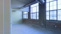 This single-floor space showcases a distinctive industrial aesthetic that blends raw architectural character with open, functional design. The interior is defined by exposed brick walls that add warmth and texture, contrasting beautifully with the smooth concrete flooring that spans the entire space. Large, multi-pane windows line the walls, flooding the interior with abundant natural light and offering views to the surrounding area. The soaring ceiling height enhances the sense of openness and volume, while exposed ductwork running overhead reinforces the loft-like, industrial character of the space. Concrete structural columns punctuate the floor plan, serving as bold architectural features that echo the building's original construction. The open layout provides exceptional flexibility, making it well-suited for a variety of uses such as creative offices, studios, showrooms, or event space. The combination of natural light, raw materials, and generous proportions creates an inspiring and dynamic ambiance throughout. The space retains much of its original industrial fabric, giving it an authentic character that is both visually striking and highly adaptable to modern needs.