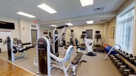 Located at 659 Rice Boulevard in Exton, Pennsylvania, this fitness center offers a well-appointed, single-floor workout facility designed to support a comprehensive exercise routine. The space features a clean, neutral interior with a drop-panel ceiling equipped with recessed fluorescent lighting that ensures bright, even illumination throughout. Large wall mirrors enhance the sense of openness and allow users to monitor their form during workouts. The fitness area is outfitted with a solid selection of strength training equipment, including a prominent multi-station cable and weight machine, a dedicated weight bench, and a variety of free weights. On the cardio side, the facility provides multiple treadmills, an upright stationary bike, and additional aerobic machines, all positioned to allow comfortable spacing between users. Stability balls and supplemental fitness accessories round out the available equipment. The flooring is low-pile carpet suited for fitness use, and the room features neutral-toned walls that contribute to a focused, no-distraction workout environment. Emergency exit access is clearly marked, and the space is neatly organized, reflecting a well-maintained facility. Overall, this fitness center provides a functional and inviting environment for residents or members seeking a convenient on-site exercise option.