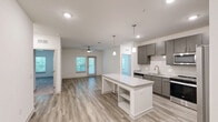 Located at 6000 Front St in Summerville, SC, this well-appointed 2-bedroom, 2-bathroom single-floor home offers a thoughtfully designed layout with modern finishes throughout. The kitchen serves as a functional centerpiece, featuring sleek gray cabinetry, granite countertops, a tiled backsplash, stainless steel appliances including a side-by-side refrigerator, electric range, and built-in microwave, along with a freestanding island with open shelving and pendant lighting overhead. Wood-look plank flooring flows throughout the main living areas, creating a clean and cohesive aesthetic. Both bedrooms are carpeted for comfort, each equipped with a ceiling fan and natural light from exterior windows. The generously sized primary bedroom connects to a private en-suite bathroom featuring granite countertops, dark cabinetry, a glass-enclosed shower, and direct access to a walk-in closet with built-in shelving. The second bathroom offers a granite vanity and a soaking tub with shower. A dedicated laundry room houses a full-size washer and dryer. Two hallways connect the space efficiently, and two closets provide ample storage. The overall aesthetic is bright, neutral, and contemporary throughout.