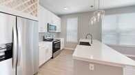 This single-floor residence presents a clean, modern aesthetic carried consistently throughout its layout. The kitchen serves as a functional centerpiece, showcasing white shaker-style cabinetry with brushed nickel hardware, crisp white quartz countertops, and a full suite of stainless steel appliances including a side-by-side refrigerator with ice and water dispenser, electric range, and over-the-range microwave. A built-in wine rack adds a decorative touch above the refrigerator, while a peninsula with an undermount sink and pendant lighting enhances both utility and style. Light wood-tone flooring runs through the kitchen and main living areas, contributing to a bright, airy atmosphere.

The bedrooms feature neutral carpet, soft gray walls, and ceiling fans, with natural light provided by windows fitted with blinds. The primary bedroom includes a walk-in closet with built-in shelving. The bathrooms are thoughtfully finished — one features a soaking tub and shower combination with large-format beige tile surround and brushed nickel fixtures, while another includes a white quartz vanity, undermount sink, and framed mirrors with built-in shelving nearby. Throughout, the home maintains a cohesive, contemporary palette ideal for comfortable living.