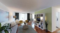 Located at 4710 Bethesda Avenue, Unit 505 in Bethesda, MD, this single-floor residence combines contemporary design with functional living. The expansive open-concept living area is anchored by rich parquet wood flooring and flooded with natural light through floor-to-ceiling sliding glass doors that lead to a private balcony. The living space is thoughtfully arranged to accommodate multiple seating and dining zones, separated by a sleek white open-shelving unit that also houses a flat-screen TV. An accent wall adds a striking visual element alongside curated artwork throughout. The kitchen features white cabinetry, a gas range, ample counter space, and a built-in sink, providing a clean and efficient layout. The primary bedroom is a serene retreat highlighted by a bold textured accent wall, warm parquet floors, and generous natural light from a large window. The second bedroom offers ample closet space with full-length bi-fold doors and tasteful wall art. A clean, tiled bathroom with a shower-tub combination completes the layout. Throughout the residence, a cohesive, modern aesthetic is maintained with neutral tones, carefully chosen furnishings, and artistic accents that create an inviting and sophisticated ambiance.