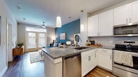 This single-story residence offers a thoughtfully designed open-concept layout that seamlessly connects the kitchen, dining, and living areas. The kitchen is a standout feature, outfitted with crisp white shaker cabinetry, granite countertops, a decorative tile backsplash, and a full suite of stainless steel appliances including a refrigerator, range, microwave, and dishwasher. A peninsula with pendant lighting serves as both a functional workspace and casual dining area. Wood-style flooring flows throughout the main living areas, complementing the warm, contemporary aesthetic.

The living area is anchored by a teal accent wall and benefits from natural light streaming through large windows and French doors, with a ceiling fan adding comfort. The bedroom continues the design language with plush carpeting, multiple windows dressed with blinds and sheer curtains, a ceiling fan, and a soothing color palette.

The bathroom is well-equipped with a granite-topped vanity, white cabinetry, wood-style flooring, and a tiled tub-shower combination. Overall, the space presents a cohesive, modern interior with quality finishes and a comfortable, functional flow.