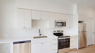 This thoughtfully designed single-floor unit offers a clean, modern aesthetic throughout its efficiently laid out living space. Light wood-tone flooring runs continuously through the unit, lending warmth and cohesion to every room.

The open-concept kitchen and living area serves as the heart of the unit. The kitchen is outfitted with crisp white flat-panel cabinetry extending nearly to the ceiling, providing generous storage. Stainless steel appliances — including an electric range, over-the-range microwave, refrigerator, and dishwasher — complement the white countertops and an undermount sink with a matte black faucet. The layout flows naturally into the living area, which is bathed in natural light from a large floor-to-ceiling window that frames scenic mountain views and opens to a private balcony.

A hallway connects the main living area to the rest of the unit, featuring a smart thermostat and access to closet storage. The bathroom is elegantly appointed with a wood-toned vanity, white countertop, undermount sink, and a tub/shower combination showcasing striking marble-look wall surrounds with brushed gold hardware, adding a refined touch to the overall design. Recessed lighting and a textured ceiling complete the space.