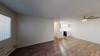 This single-floor residence offers a clean, functional layout with a cohesive design throughout. Dark wood-style flooring runs continuously across all rooms, providing a warm and grounded aesthetic that contrasts with the bright white walls and textured ceilings found throughout the space.

The open living area is spacious and versatile, illuminated by a ceiling fan with an integrated light fixture. It flows seamlessly into the kitchen, which is separated by a half-wall partition. The kitchen is well-appointed with white cabinetry, light stone-style countertops, an electric range with overhead ventilation hood, and a refrigerator, making it both practical and easy to maintain.

The bedroom is a comfortable, well-lit room featuring a large window fitted with vertical blinds that allows natural light to fill the space. A baseboard heating unit ensures year-round comfort. The window offers a view of the surrounding building exterior and landscaping.

The bathroom is neatly appointed with a single-sink vanity featuring warm wood cabinetry and a white countertop, a large wall mirror, and a full shower-tub combination. Wood-style flooring continues into this space, maintaining the unit's consistent design language throughout. Overall, the residence presents a clean, move-in ready environment with a straightforward and practical layout.
