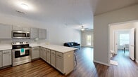 Located at 120 W Fowler Ave in West Lafayette, Indiana, this one-bedroom, one-bathroom unit offers a well-designed, single-floor layout with a functional and modern interior. The open-concept living and kitchen area serves as the heart of the home, featuring rich wood-style flooring that extends throughout the entire unit. The kitchen is equipped with a full suite of stainless steel appliances — including a refrigerator, range, microwave, and dishwasher — complemented by gray shaker-style cabinetry, white countertops, and a peninsula island with bar seating, ideal for casual dining or workspace. The living area is bright and open, with a ceiling fan and a glass exterior door that brings in natural light and provides access to a private balcony. The bedroom is a comfortable, well-proportioned space with windows on multiple walls, allowing ample natural light, and opens conveniently to the rest of the unit. The bathroom features a gray vanity with a white countertop and a large mirror with overhead lighting. A dedicated laundry room with a full-size washer and dryer adds everyday convenience. A textured ceiling runs throughout the unit, adding a subtle design detail to the clean, neutral palette.