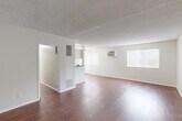 This single-floor unit offers a clean, functional layout with a bright and open feel throughout. Rich, dark hardwood flooring flows consistently across all rooms, providing a warm contrast to the crisp white walls and textured ceilings found throughout the space.

The expansive living area is bathed in natural light from multiple windows fitted with vertical blinds, creating an airy atmosphere. A wall-mounted air conditioning unit ensures year-round comfort. The open layout connects seamlessly to a peninsula-style counter that separates the living space from the kitchen, offering a convenient pass-through area.

The galley kitchen is efficiently designed with white cabinetry, granite-style countertops, a double basin sink, and a gas range with an overhead microwave. The layout maximizes functionality within a compact footprint.

Two well-proportioned bedrooms each feature hardwood flooring, neutral walls, and windows that allow natural light to filter in. One bedroom includes a sliding closet, while both offer comfortable, versatile spaces.

The bathroom is thoughtfully appointed with white cabinetry, a granite countertop vanity, a mirrored medicine cabinet, and a full tiled tub and shower surround accented with decorative tile insets. Hardwood flooring continues into the bathroom, maintaining a cohesive design throughout the unit.