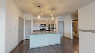 This well-appointed 2-bedroom, 2-bathroom residence offers a thoughtfully designed single-floor layout that balances modern style with everyday functionality. The open-concept living area features rich wood-look hardwood flooring and a ceiling fan, with natural light streaming in through multiple windows fitted with blinds, creating a bright and welcoming atmosphere.

The kitchen is a standout feature, showcasing a large central island with granite countertops and an undermount sink, complemented by light wood cabinetry, dark lower cabinets, and a decorative mosaic tile backsplash. Stainless steel appliances — including a refrigerator, electric range, and over-the-range microwave — complete the space, while pendant lighting adds a contemporary touch overhead.

Both bedrooms offer plush wall-to-wall carpeting and neutral tones, with one bedroom featuring elevated transom-style windows that allow natural light while maintaining privacy. The two bathrooms are finished with large-format gray tile, one featuring a soaking tub and the other a frameless sliding glass shower enclosure, both with wood-look flooring and clean, modern fixtures.

Throughout the residence, a consistent palette of warm neutrals, contemporary finishes, and durable materials creates a cohesive and move-in-ready living environment.