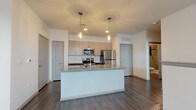 This well-appointed 2-bedroom, 2-bathroom residence offers a thoughtfully designed single-floor layout that balances modern style with everyday functionality. The open-concept living area features rich wood-look hardwood flooring and a ceiling fan, with natural light streaming in through multiple windows fitted with blinds, creating a bright and welcoming atmosphere.

The kitchen is a standout feature, showcasing a large central island with granite countertops and an undermount sink, complemented by light wood cabinetry, dark lower cabinets, and a decorative mosaic tile backsplash. Stainless steel appliances — including a refrigerator, electric range, and over-the-range microwave — complete the space, while pendant lighting adds a contemporary touch overhead.

Both bedrooms offer plush wall-to-wall carpeting and neutral tones, with one bedroom featuring elevated transom-style windows that allow natural light while maintaining privacy. The two bathrooms are finished with large-format gray tile, one featuring a soaking tub and the other a frameless sliding glass shower enclosure, both with wood-look flooring and clean, modern fixtures.

Throughout the residence, a consistent palette of warm neutrals, contemporary finishes, and durable materials creates a cohesive and move-in-ready living environment.