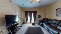 This single-floor residence offers a well-organized layout with distinct living, dining, kitchen, sleeping, and bathroom areas, all finished in warm neutral tones that create a cohesive and inviting atmosphere throughout.

The living room is a comfortable gathering space, featuring carpet flooring, a ceiling fan, and a large window dressed with dark curtains that frame natural light. The room accommodates a leather reclining sofa, a flat-screen television, and a textured area rug anchoring the space.

Adjacent to the entry, the dining area features tile flooring and an elegant chandelier overhead, with a round dark wood table and matching chairs creating an intimate setting for meals. Framed wall art adds a decorative touch to the space.

The galley-style kitchen is efficiently designed with warm wood cabinetry, dark granite-style countertops, and tile flooring. It is equipped with stainless steel appliances including a range, microwave, and refrigerator, with ample storage on both sides.

Both bedrooms are carpeted and include ceiling fans, windows with natural light, and closet access. Each room comfortably fits a bed and desk workspace, making them functional for both rest and productivity.

The two bathrooms feature tile flooring, warm wood vanity cabinetry, dark granite-style countertops, and large mirrors, providing practical and well-appointed spaces for daily use.