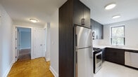 Located at 3 Davenport Ave in New Rochelle, NY, this thoughtfully renovated single-floor residence combines modern finishes with classic architectural details. The open layout is unified by warm parquet hardwood flooring throughout the living areas and bedrooms, lending a timeless character to the space.

The kitchen has been fully updated and features dark espresso-toned cabinetry with matte black hardware, contrasting crisp white countertops, and a full suite of stainless steel appliances including a gas range, over-the-range microwave, and refrigerator. A window above the sink allows natural light to brighten the workspace, while the efficient L-shaped layout maximizes functionality.

The living area is spacious and bright, with light gray walls and the same classic parquet flooring. Multiple windows invite abundant natural light and offer views of surrounding greenery. The bedroom includes a sliding-door closet with double hanging rods for ample storage, and its own windows framing outdoor views.

The bathroom is elegantly appointed with floor-to-ceiling marble-style tile surrounding the tub and shower combination, complemented by a glass panel enclosure, a sleek modern vanity, and a frosted privacy window. Throughout the unit, clean white trim and panel doors contribute to a polished, cohesive aesthetic.