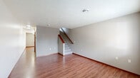 This two-story residence in Sioux Falls, South Dakota, offers a practical and well-organized layout spread across two floors. The main level features an open living room with warm hardwood-style flooring, neutral-toned walls, and a textured ceiling, with a staircase accented by a wood handrail leading to the upper level. Natural light filters in through a window overlooking the surrounding neighborhood. The kitchen is thoughtfully designed with rich oak cabinetry, laminate countertops, and stainless steel appliances including a refrigerator, electric range, over-the-range microwave, and dishwasher, all set atop hardwood-style flooring. A half bathroom on the main level features matching oak cabinetry and hardwood-style flooring. Upstairs, two carpeted bedrooms provide comfortable living spaces, each with windows that bring in natural light and views of the surrounding area. The primary bedroom offers a cozy, well-proportioned layout. A full bathroom on the upper level includes a tub-shower combination with clean white finishes. Wood-trimmed doors and warm baseboards carry a consistent design throughout the home, lending a cohesive and inviting feel to the entire space.