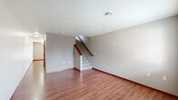 This two-story residence in Sioux Falls, South Dakota, offers a practical and well-organized layout spread across two floors. The main level features an open living room with warm hardwood-style flooring, neutral-toned walls, and a textured ceiling, with a staircase accented by a wood handrail leading to the upper level. Natural light filters in through a window overlooking the surrounding neighborhood. The kitchen is thoughtfully designed with rich oak cabinetry, laminate countertops, and stainless steel appliances including a refrigerator, electric range, over-the-range microwave, and dishwasher, all set atop hardwood-style flooring. A half bathroom on the main level features matching oak cabinetry and hardwood-style flooring. Upstairs, two carpeted bedrooms provide comfortable living spaces, each with windows that bring in natural light and views of the surrounding area. The primary bedroom offers a cozy, well-proportioned layout. A full bathroom on the upper level includes a tub-shower combination with clean white finishes. Wood-trimmed doors and warm baseboards carry a consistent design throughout the home, lending a cohesive and inviting feel to the entire space.