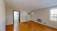 This efficient one-bedroom, one-bathroom unit is thoughtfully laid out across a single floor, offering a practical and comfortable living arrangement. The living room serves as the heart of the space, showcasing warm-toned hardwood floors that extend throughout, recessed lighting in the ceiling, and a white entry door with a charming arched transom window that allows natural light to filter in. A wall-mounted HVAC unit and baseboard heating provide year-round climate control, while a window along the side wall adds to the brightness of the room.

The kitchen is well-equipped, featuring rich wood cabinetry, granite countertops, a stainless steel sink, a full-size stainless steel refrigerator, and a dark tile backsplash that adds visual contrast. Tile flooring grounds the kitchen space.

The bedroom is a cozy, well-proportioned room with the same gleaming hardwood floors, a ceiling fan with light fixture, and access to a closet. The hallway connects the rooms efficiently.

The bathroom is finished with classic white subway tiles accented by a bold black tile border, a wood-toned vanity with a white basin, and a shower-tub combination. Wood-look tile flooring completes the clean, modern aesthetic of this well-maintained space.