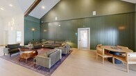 Located at 2250 Hard Scrabble Rd in Columbia, SC, this single-floor space offers a thoughtfully designed interior that blends rustic charm with contemporary style. The space is defined by its dramatic vaulted ceilings adorned with exposed dark wood beams, skylights that flood the interior with natural light, and vertical shiplap walls finished in a rich forest green — creating a warm yet sophisticated atmosphere throughout.

The expansive living room serves as the heart of the space, featuring light-toned hardwood flooring, plush seating arrangements, and a stunning large-scale nature-inspired mural that serves as a striking focal point. Multiple French doors line the walls, offering views to the outdoors and inviting abundant natural light. Warm wall sconces and pendant lighting complement the natural illumination, adding ambiance throughout the day and evening.

The kitchen is equally impressive, showcasing dark wood cabinetry topped with light quartz countertops, a stainless steel sink, and an eye-catching shiplap tile backsplash. Open black shelving with brass hardware displays decorative greenery, adding a fresh, organic touch. A bar counter with leather barstools provides additional seating, making the kitchen both functional and inviting for social gatherings.