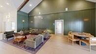 Located at 2250 Hard Scrabble Rd in Columbia, SC, this single-floor space offers a thoughtfully designed interior that blends rustic charm with contemporary style. The space is defined by its dramatic vaulted ceilings adorned with exposed dark wood beams, skylights that flood the interior with natural light, and vertical shiplap walls finished in a rich forest green — creating a warm yet sophisticated atmosphere throughout.

The expansive living room serves as the heart of the space, featuring light-toned hardwood flooring, plush seating arrangements, and a stunning large-scale nature-inspired mural that serves as a striking focal point. Multiple French doors line the walls, offering views to the outdoors and inviting abundant natural light. Warm wall sconces and pendant lighting complement the natural illumination, adding ambiance throughout the day and evening.

The kitchen is equally impressive, showcasing dark wood cabinetry topped with light quartz countertops, a stainless steel sink, and an eye-catching shiplap tile backsplash. Open black shelving with brass hardware displays decorative greenery, adding a fresh, organic touch. A bar counter with leather barstools provides additional seating, making the kitchen both functional and inviting for social gatherings.