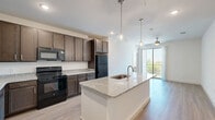 Located in Denton, TX, this well-appointed 3-bedroom, 2-bathroom single-story home offers a thoughtfully designed open-concept layout. The combined kitchen and living area serves as the heart of the home, anchored by a large granite-topped island with an undermount sink and stylish pendant lighting overhead. Rich dark-toned cabinetry lines the kitchen walls, providing ample storage, while light wood-look flooring and black appliances complete the modern aesthetic. The living area flows naturally toward a sliding glass door that opens to a private balcony, offering outdoor views and natural light. The primary bedroom features hardwood-style flooring, a ceiling fan, and direct access to the balcony. Its en-suite bathroom includes a dual-sink granite vanity with dark cabinetry and leads to a spacious walk-in closet outfitted with wire shelving systems. The two additional bedrooms are carpeted, include ceiling fans, and are brightened by windows with outdoor views. The second bathroom is clean and functional, featuring a granite vanity, tiled tub-shower combo, and light wood-look flooring. A dedicated laundry room and utility space add further practicality to this efficiently planned home.