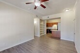 Located at 6929 Commerce Cir in Baton Rouge, Louisiana, this one-bedroom, one-bathroom unit offers a well-organized and functional single-floor layout. The open-concept living and kitchen area serves as the heart of the home, featuring durable hardwood-style flooring, crown molding, and a ceiling fan with light fixture. Natural light flows in through multiple windows and a glass-paned door that opens to the exterior, creating a bright and welcoming atmosphere. The kitchen is thoughtfully appointed with warm wood cabinetry, granite-style countertops, black appliances including a range, microwave, and refrigerator, and a stainless steel sink. Open shelving adjacent to the kitchen provides additional storage and display space. The bedroom offers a comfortable retreat with plush carpeting, a window for natural light, and access to a spacious walk-in closet equipped with wire shelving and hanging rods. The bathroom includes a full soaking tub with overhead storage and direct access to the laundry area, which accommodates a full-size side-by-side washer and dryer. Neutral tones throughout the unit create a clean, versatile backdrop suitable for a variety of interior styles.