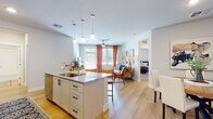 This thoughtfully designed single-floor residence offers a cohesive open-concept layout where the kitchen flows seamlessly into the living and dining areas. The kitchen serves as a central hub, featuring white shaker cabinetry, granite countertops, stainless steel appliances, and a large island with an integrated sink and bar seating illuminated by pendant lighting. Light wood-style flooring extends throughout the main living areas, enhancing the bright, airy atmosphere.

The dining area accommodates a round wooden table with upholstered chairs, accented by decorative wall mirrors and artwork. The living space is bathed in natural light through large windows dressed with warm drapery and a ceiling fan overhead.

Both bedrooms are carpeted and generously sized, each equipped with ceiling fans and ample natural light from windows with blind and drape combinations. The primary bedroom includes access to a walk-in closet. Each bedroom is served by its own bathroom — the primary bath features a glass-enclosed walk-in shower and a granite double vanity, while the secondary bath offers a tiled shower-tub combination with hardwood-style flooring and a granite vanity. The overall aesthetic is clean, contemporary, and cohesive throughout.
