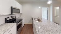 This single-floor residence offers a clean, modern interior designed for comfortable everyday living. The open-concept kitchen serves as a central highlight, featuring granite countertops, crisp white cabinetry, and a full suite of stainless steel appliances including a refrigerator, electric range, and microwave. A peninsula with an integrated sink and pendant lighting above adds both functionality and style, while rich dark hardwood-style flooring runs throughout the main living and kitchen areas, lending warmth and continuity to the space.

The living area is generously proportioned, finished with the same hardwood-style flooring and a ceiling fan, creating an inviting and practical setting. Bedrooms are fitted with plush carpeting and ceiling fans, offering a comfortable retreat. Natural light filters through slatted window blinds in the bedrooms, contributing to a bright and airy atmosphere. The bathroom is finished with a clean white palette, featuring a full soaking tub with shower, granite-topped vanity, and hardwood-style flooring that carries through from the main living areas. Throughout the space, neutral wall tones, clean white trim, and consistent finishes create a cohesive and move-in-ready environment.