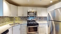 Located at 2000 Riverside Dr in Richmond, Virginia, this single-floor residence offers a thoughtfully designed layout with modern finishes throughout. The kitchen is a standout feature, equipped with stainless steel appliances including a gas range, over-the-range microwave, dishwasher, and refrigerator. White shaker-style cabinetry provides ample storage, while granite countertops and a grey subway tile backsplash add a polished, contemporary aesthetic. Track lighting illuminates the workspace, and a peninsula counter extends the prep area while creating a natural transition to the open living space. The living area is bright and airy, benefiting from a floor-to-ceiling sliding glass door that opens onto a private balcony, allowing natural light to pour in across the hardwood-style flooring. The bedroom is generously proportioned with the same hardwood-style flooring and easy access to a hallway corridor. The bathroom features a sliding glass enclosed shower, a vanity with storage, and clean, neutral finishes. Throughout the residence, light grey walls, white trim, and textured ceilings contribute to a cohesive and understated design that is both functional and inviting.