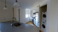 Located at 205 Church Street in the heart of New Haven, CT, this two-bedroom, two-bathroom residence offers a generous and well-appointed single-floor layout. The space is designed with functionality and comfort in mind, making efficient use of its expansive footprint.

The kitchen is a standout feature, showcasing sleek grey countertops, white shaker-style cabinetry, and stainless steel appliances including a gas range, microwave, and full-size refrigerator. A deep undermount sink is positioned at the peninsula, which provides additional prep space and a natural separation between the kitchen and living areas. Natural light filters in through a window fitted with blinds, brightening the space. Warm hardwood flooring runs throughout, adding a classic and cohesive aesthetic.

A particularly practical highlight is the in-unit stacked washer and dryer, conveniently tucked into a dedicated closet adjacent to the kitchen — a sought-after amenity. The overall layout flows smoothly across the single floor, with the two bedrooms and two full bathrooms offering ample accommodation for residents. Clean white walls, pendant lighting, and thoughtful storage solutions contribute to a bright, organized, and move-in-ready atmosphere throughout the home.