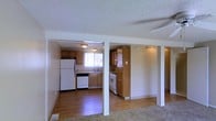 This 2-floor space offers a practical and welcoming layout defined by a blend of hard and soft flooring surfaces. The main level showcases a combination of warm hardwood flooring in the kitchen and surrounding areas, transitioning into carpeting in the living space. A textured popcorn ceiling runs throughout, adding a classic character to the interior.

The kitchen is well-appointed with honey-toned wood cabinetry that provides generous storage across both upper and lower cabinets, including a tall pantry-style cabinet for additional organization. White appliances, including a refrigerator, dishwasher, and range, complement the light-colored countertops and simple sink setup positioned near a window that allows natural light to filter in. The open sightlines between the kitchen and adjacent areas create a connected, airy feel throughout the main level.

Structural columns subtly define the transition between spaces without fully closing off the floor plan, preserving the open nature of the layout. Ceiling-mounted light fixtures provide consistent illumination throughout. The overall ambiance is functional and straightforward, offering a clean, move-in ready environment across both levels.